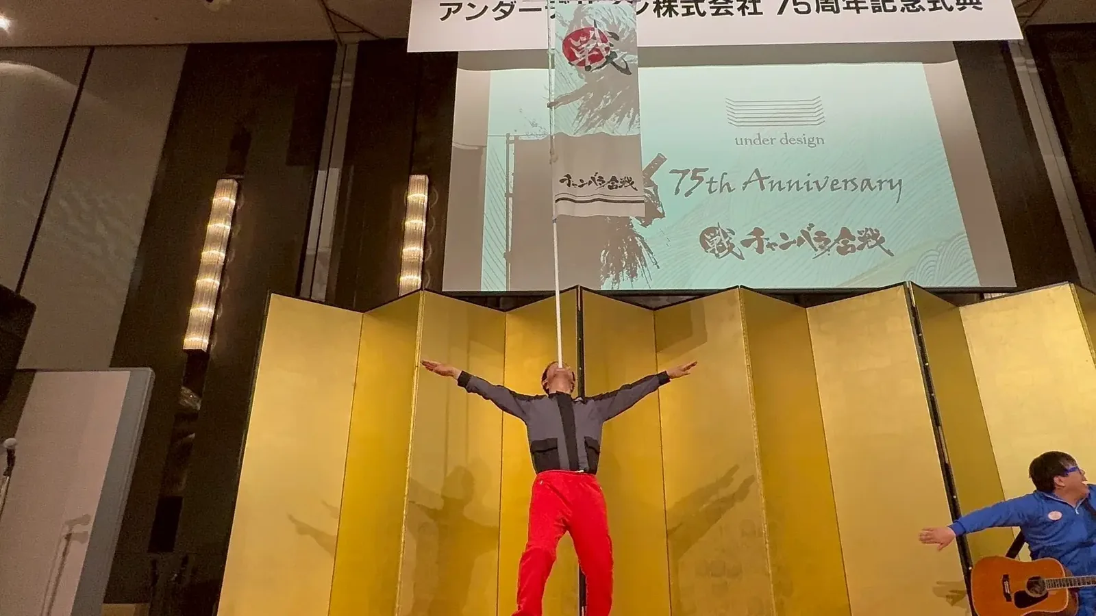 アンダーデザイン様のユニフォームを着用し、顎にのぼり旗を乗せるテツさん