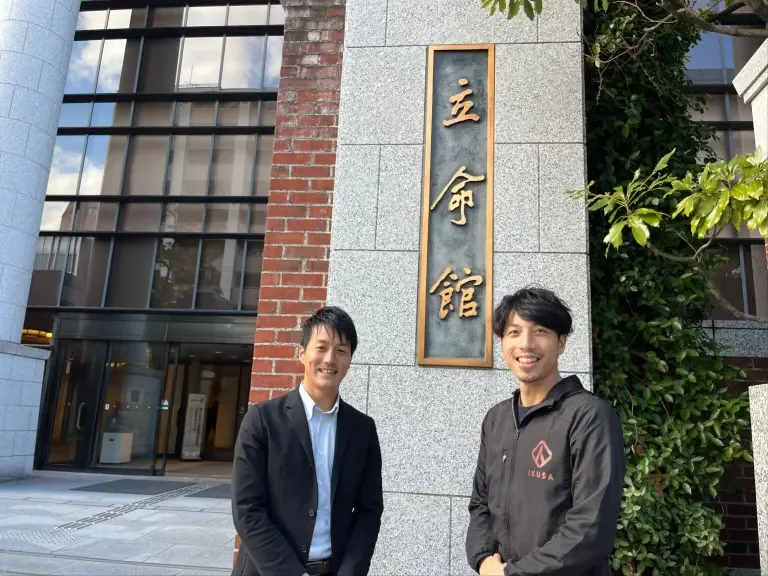 立命館の校名板の前に立つご担当者様とIKUSAスタッフ